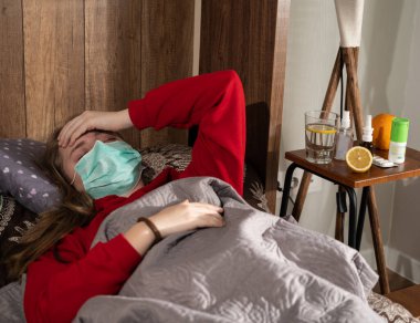 Sağlık ve tıbbi konsept. Maskeli hasta genç kız evde yatakta yatıyor. 