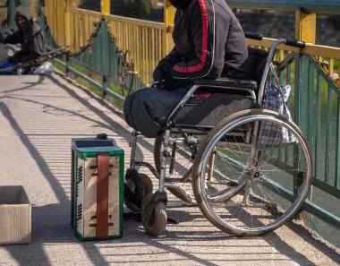 UZHHOROD, UKRAINE - APRIL 10, 2020: Homeless man in wheel chair begging for alms on a city street of Uzhhorod, Ukraine clipart