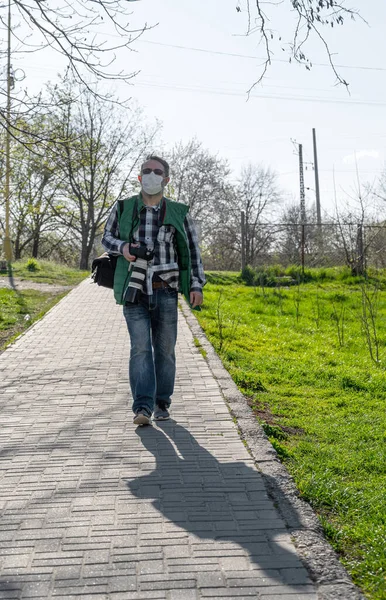 美しい春の日にコロナウイルスの流行の間に捨てられた通りの医療マスクの高齢者写真家 — ストック写真