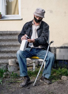 Sağlık ve tıbbi konsept. Koruyucu maskeli kıdemli bir adam dışarıda bir şişe el dezenfektanı tutuyor.
