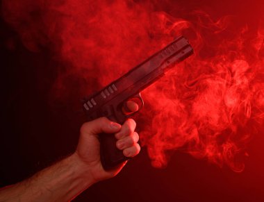 Kırmızı dumanlı arka planda silah tutan bir adam.