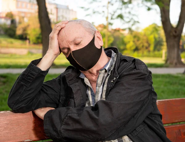 Senior man in facial mask suffering from headache outdoors