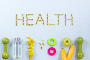 Sağlık kelimesi, spor aletleri, zemin pulları, su ve meyvelerle çevrili omega 3 kapsülleriyle yazılmıştır. Sağlıklı yaşam tarzı konsepti, kilo kaybı