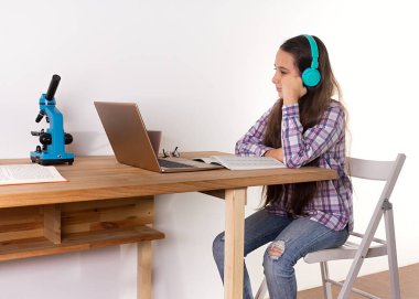 Uzaktan öğrenme. Evde eğitim, dizüstü bilgisayarda okuyan, kulaklıkla müzik dinleyen bilim ve biyoloji yapan genç bir kız. Öğrenme konsepti.