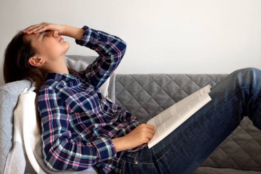 Çevrimiçi eğitim ve çalışma mesafesi. Kanepede oturup kitap okuyan yorgun bir kız..