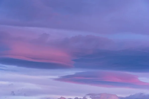 Lenticular clouds over the sky at dawn with reddish and orange colors