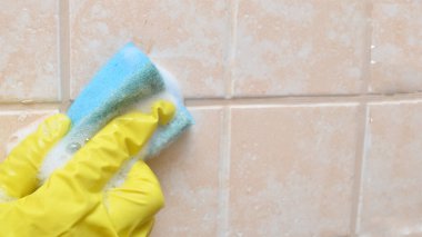 Sarı koruyucu eldivenli bir adam banyoda kirli seramik fayanslar yıkıyor. Ödev afişi..
