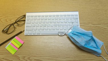 Beyaz bilgisayar klavyesi, fare, kalem, maske, gözlük ve atölye kahverengi ahşap masa üzerindeki renkli kağıt postit. iş için evden ya da WFH