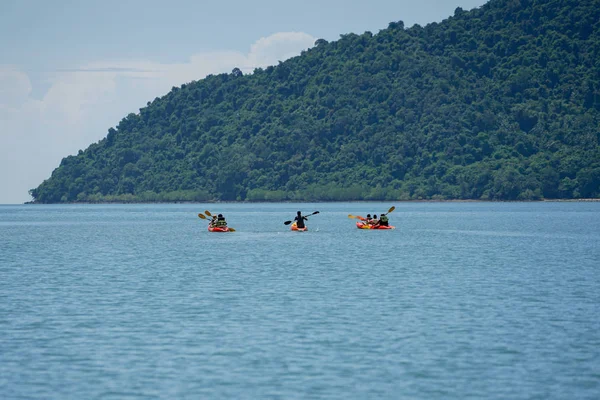 Enfoque selectivo en grupo de viajeros que navegan en canoa por la superficie del mar para recorrer con paisajes marinos e islas de fondo — Foto de Stock