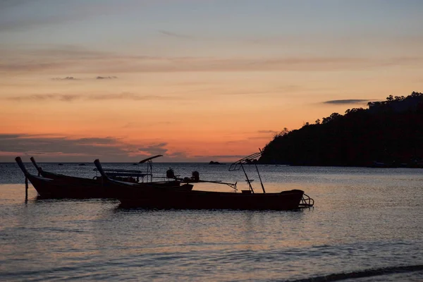 Grupo de siluetas de barcos de cola larga tradicionales flotando en el mar con crepúsculo de puesta de sol e isla en el fondo — Foto de Stock