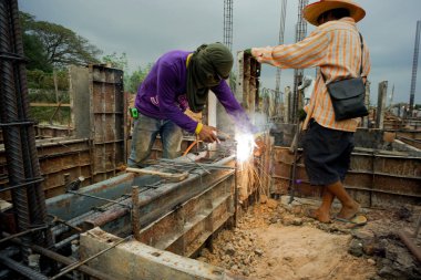 İnşaat alanındaki beton yapı modelini desteklemek için çeliği kaynaklayan işçiler