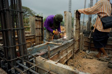 İnşaat alanındaki beton yapı modelini desteklemek için çeliği kaynaklayan işçiler