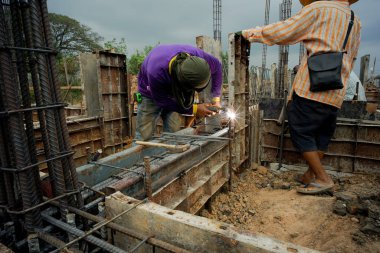 İnşaat alanındaki beton yapı modelini desteklemek için çeliği kaynaklayan işçiler