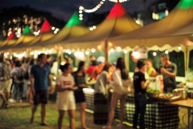 Bulanık hareketli insanlar gece yemek festivalinde arka planda dekoratif bokeh ışıklarıyla yürüyorlar.
