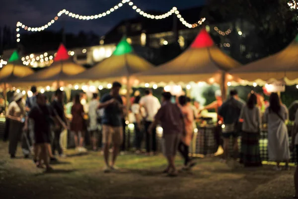 Bulanık hareketli insanlar gece yemek festivalinde arka planda dekoratif bokeh ışıklarıyla yürüyorlar.