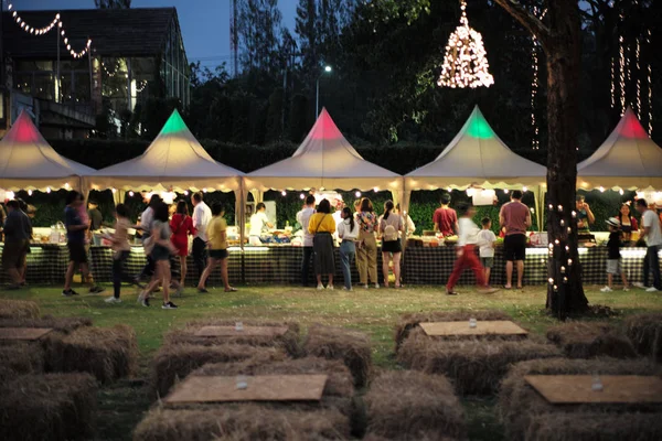 Bulanık hareketli insanlar gece yemek festivalinde arka planda dekoratif bokeh ışıklarıyla yürüyorlar.