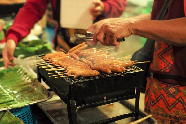 Close-up rij van vlees worsten op de metalen grill met beweging wazig handen en verkoper op de achtergrond — Stockfoto