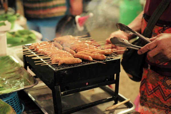 Close-up rij van vlees worsten op de metalen grill met beweging wazig handen en verkoper op de achtergrond — Stockfoto