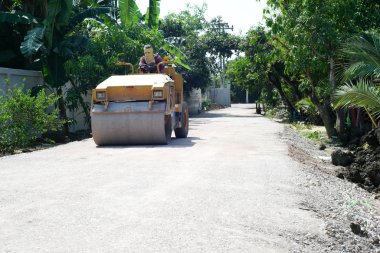 İşçi, çarpışan taş yolda yüzeyi hazırlamak için yol silindirini kullanır