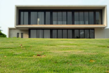 Arka planda odaklı olmayan modern mimari tarzlı ev ile ön planda çimen alanı