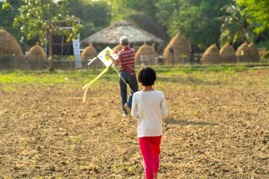 Küçük Asyalı kız ve büyükbabanın arka portresi şehir parkında geleneksel uçurtma çalıyor.