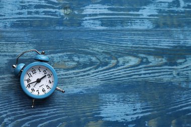 Mavi ahşap zemin üzerinde beyaz kadranlı mavi çalar saat.
