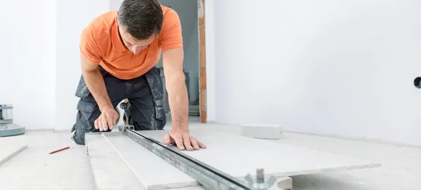 man cutting ceramic tiles with handy machine at the construction site indoors