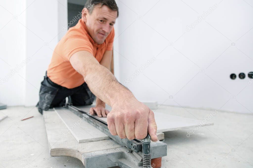 man cutting ceramic tiles with handy machine at the construction site indoors