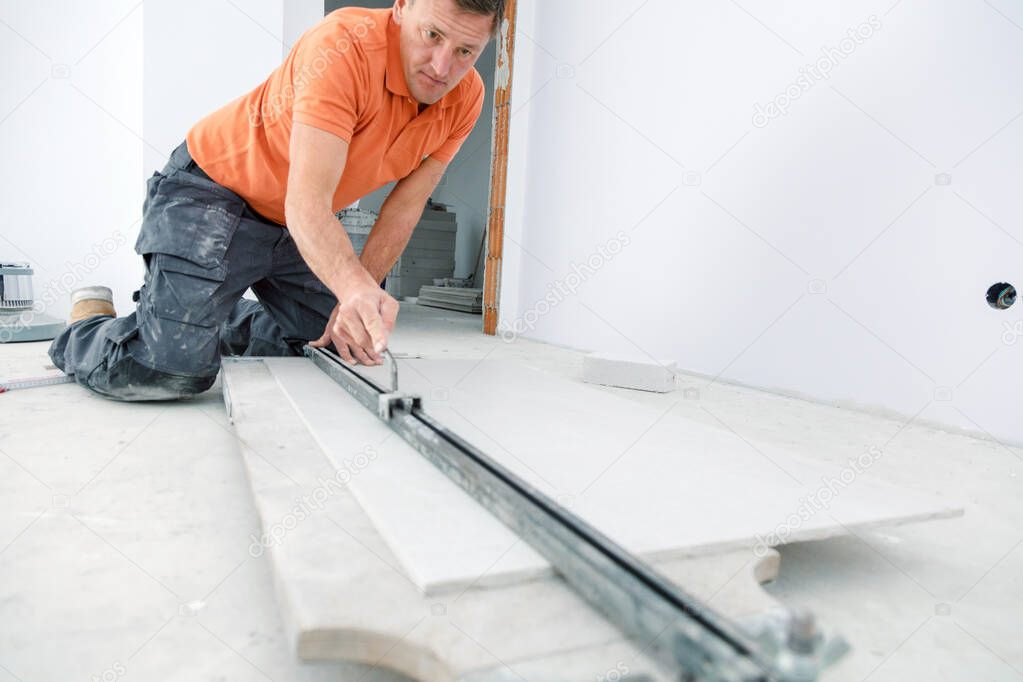 Workman cutting ceramic tiles with handy machine at the construction site indoors