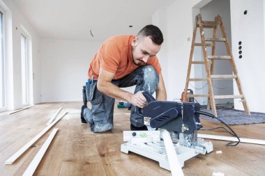 Kesik testereli bir adam inşaat alanında etek tahtaları kesiyor.. 