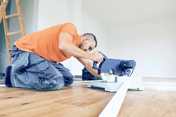 worker cutting skirting boards on a construction site. Lay parquet floor