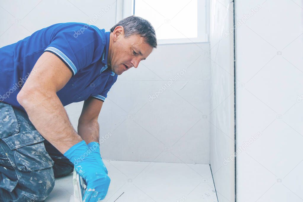 middle aged man grouting ceramic tiles on the floor 