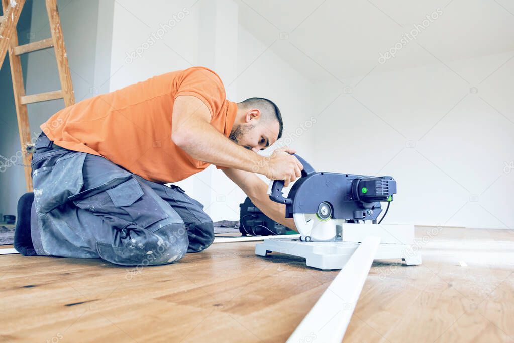 worker cutting skirting boards on a construction site. Lay parquet floor