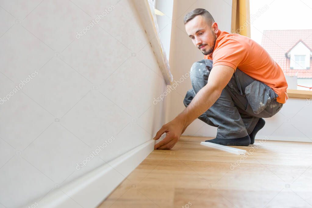male worker cutting skirting boards on a construction site. Lay parquet floor  