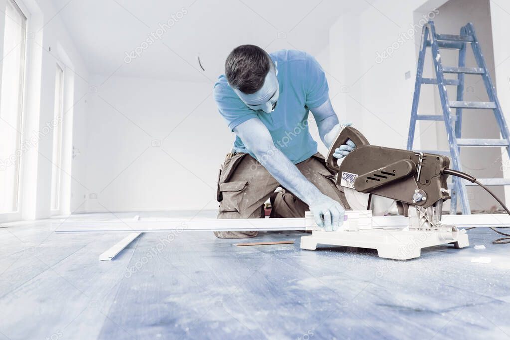 man with a chop saw cutting skirting boards on a construction site. Lay parquet floor