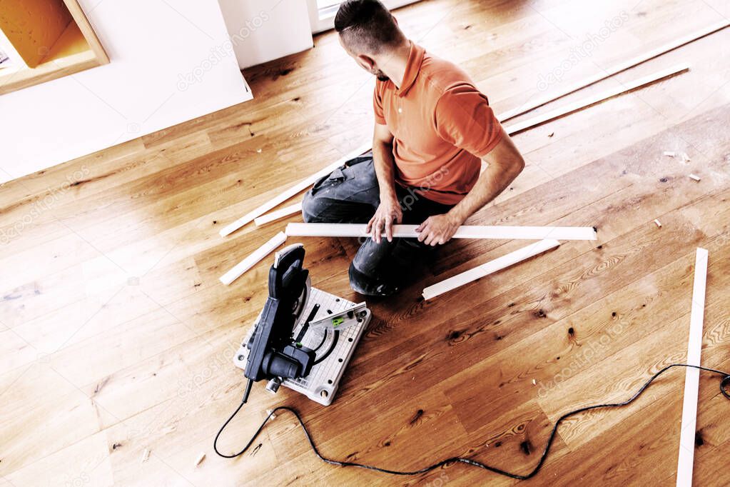 high angle view of man with a chop saw cutting skirting boards on a construction site. Lay parquet floor