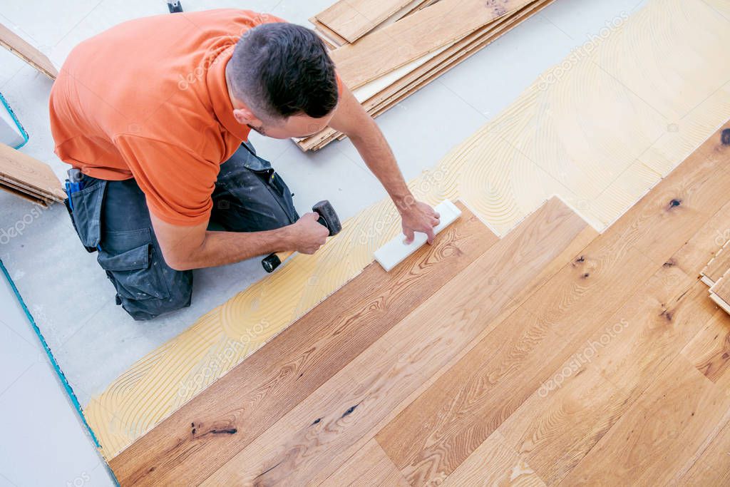 high angle view of male worker installing parquet floor on construction site. Lay parquet floor  