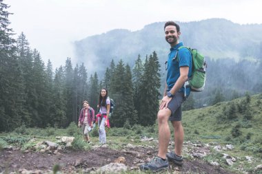 Sisli bir günde güzel dağlarda yürüyüş yapan sırt çantalı genç arkadaşlar.