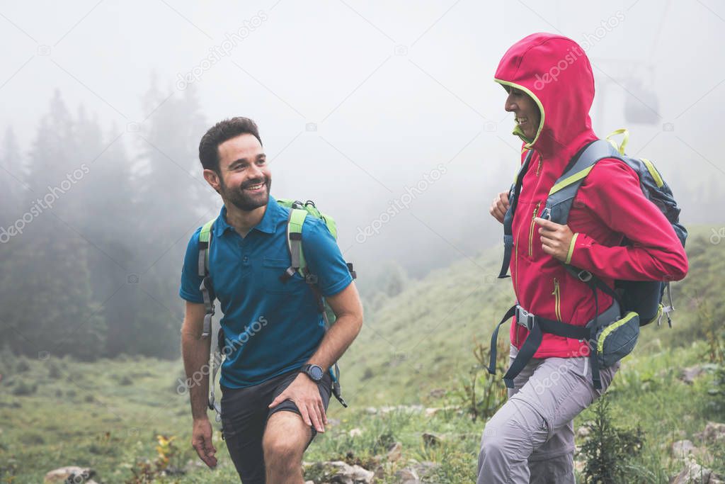 young friends with backpacks hiking in beautiful mountains at foggy day