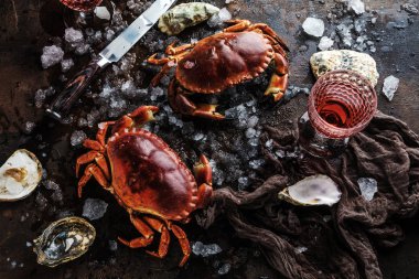 close-up view of crabs, oysters and knife with ice on dark surface 
