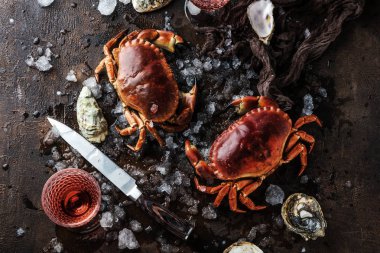 top view of crabs, oysters and ice with knife on dark surface