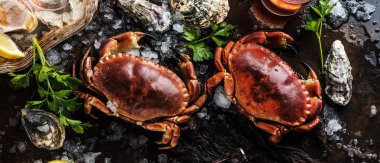 top view of crabs and oysters with ice and herbs on dark surface  