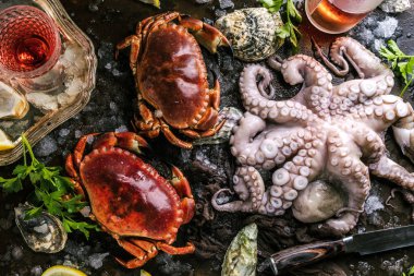 top view of crabs, octopus and oysters with ice and herbs on dark surface  