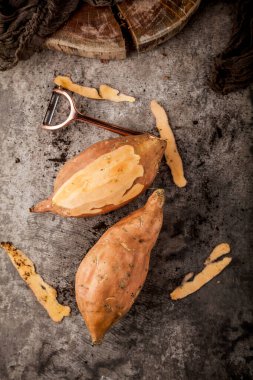 top view of tasty healthy whole sweet potatoes and peeler on grey surface