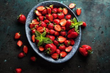 Gri yüzeyde taze olgun çileklerin olduğu kasenin üst görüntüsü.