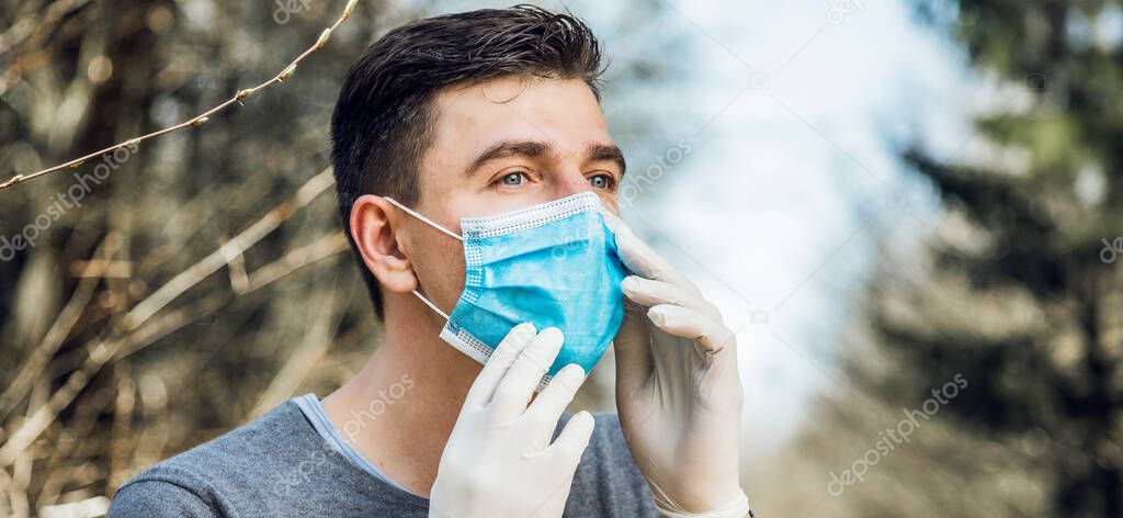 young man wearing protective gloves and sterile medical mask while walking in park. coronavirus protection concept