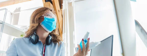 young woman in medical mask working from home and choosing sanitizers