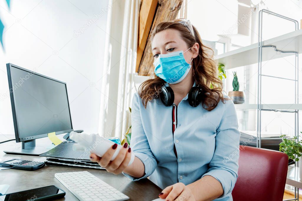 young woman in medical mask working from home and holding sanitizers
