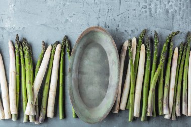 Taze organik yeşil ve beyaz kuşkonmaz manzarası ve gri arka planda boş tabak. 