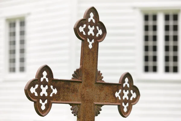 Rusted cemetery cross and white wooden church out of focus. — Stock Photo, Image